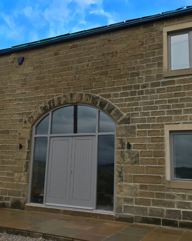 Exterior view of arched patio doors with timber panels in traditional stone building