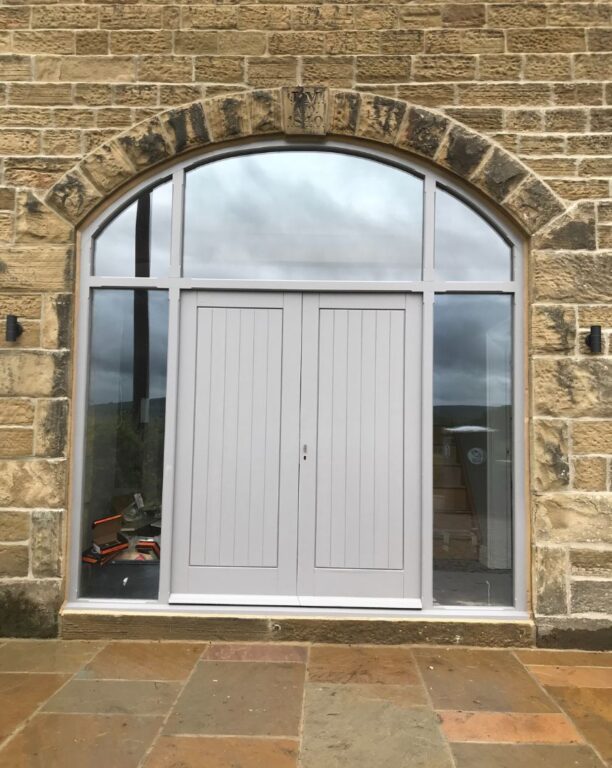 Grey timber French doors with sidelights fitted in stone archway opening