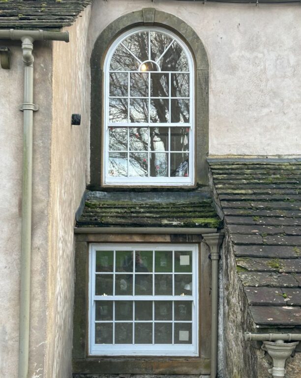 Traditional arched sash window with glazing bars in period stone cottage with slate roof