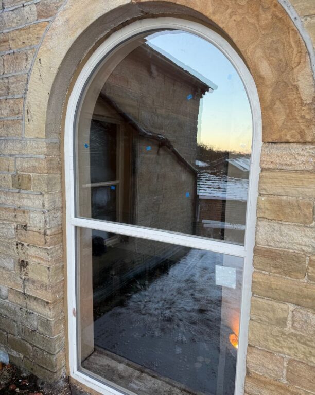 Arched window with white frame set in traditional sandstone wall surround