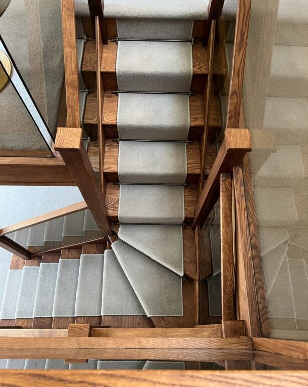Oak staircase with grey carpet runner and glass panel handrail viewed from above by Overgreen Joinery