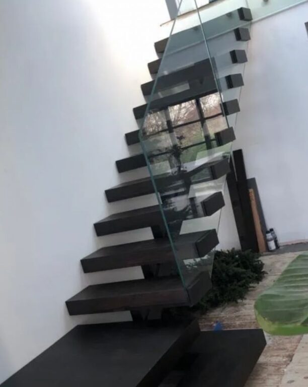 Modern floating staircase with dark wood treads and structural glass balustrade by Overgreen Joinery