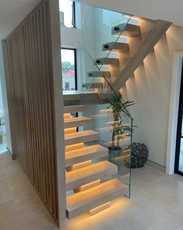 Modern staircase with integrated LED step lighting, glass balustrade and timber slat feature wall by Overgreen Joinery