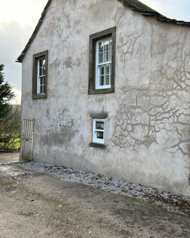 Period cottage windows with stone lintels and white frames in rendered walls