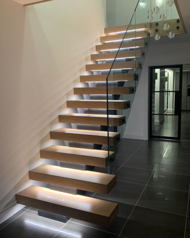 Contemporary floating oak staircase with integrated LED step lighting and glass balustrade by Overgreen Joinery