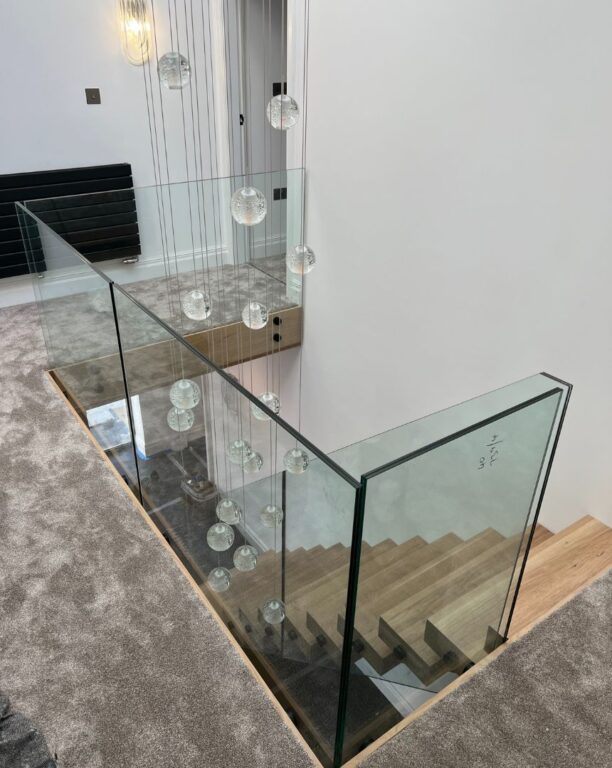 Contemporary staircase with structural glass balustrade and statement pendant lighting by Overgreen Joinery