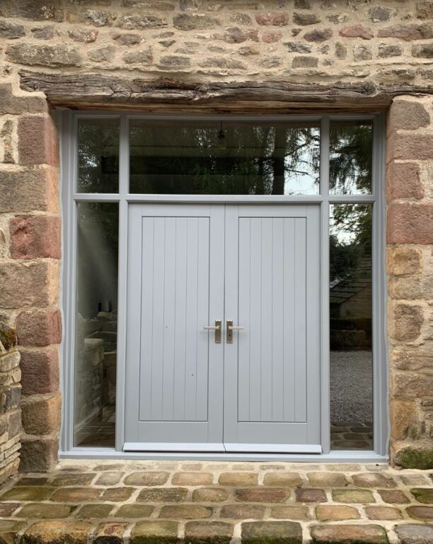 Grey French doors with sidelights and rustic timber lintel in traditional stone cottage
