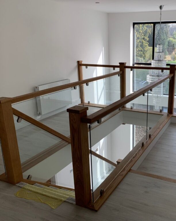 Oak landing balustrade with glass panels overlooking entrance hallway by Overgreen Joinery
