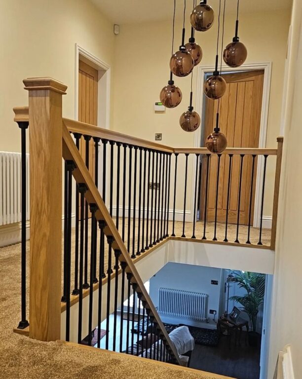 Oak staircase with black metal spindle balustrade and bronze pendant lighting by Overgreen Joinery