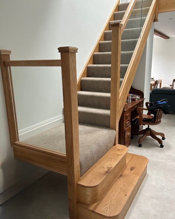 Traditional oak staircase with curved bottom steps and grey carpet runner by Overgreen Joinery