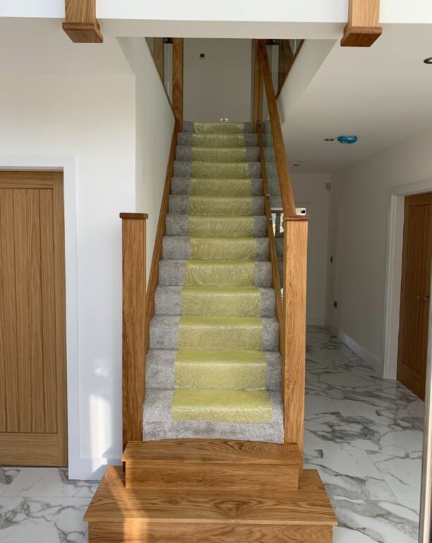Traditional oak staircase with curved bottom steps on marble floor with protective covering by Overgreen Joinery