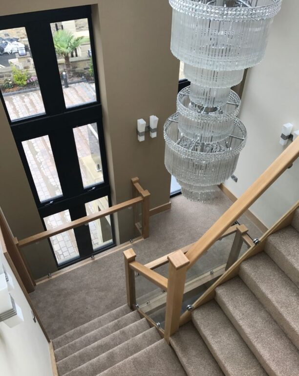 Oak staircase with glass balustrade overlooking entrance hall with statement chandelier by Overgreen Joinery