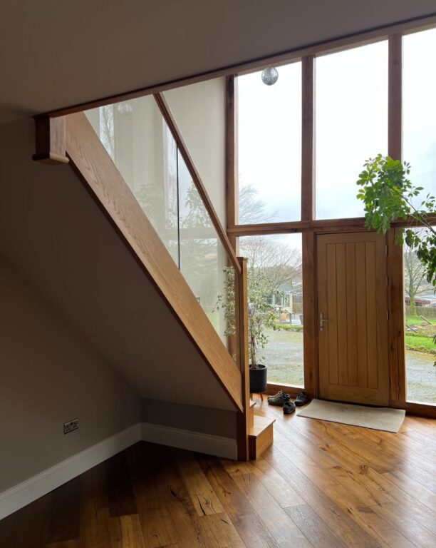 Oak staircase with glass balustrade in modern home with floor-to-ceiling windows by Overgreen Joinery