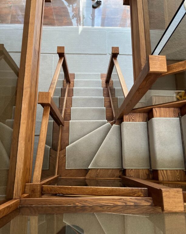 Oak staircase with glass panel balustrade and grey carpet runner viewed from above by Overgreen Joinery