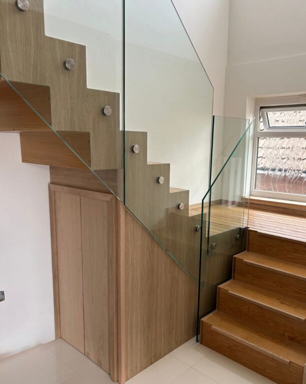 Contemporary oak staircase with glass balustrade and integrated understair storage cupboards by Overgreen Joinery