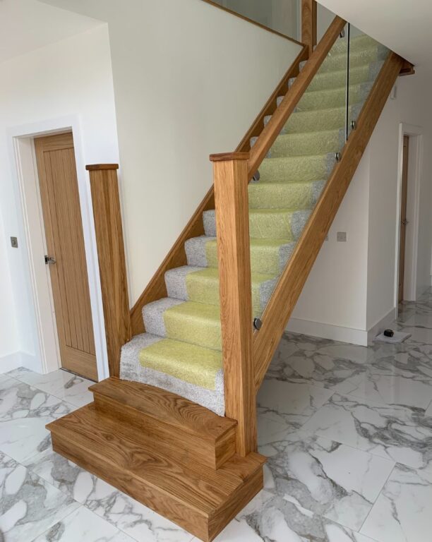 Oak staircase with glass panel balustrade on marble flooring with protective covering by Overgreen Joinery