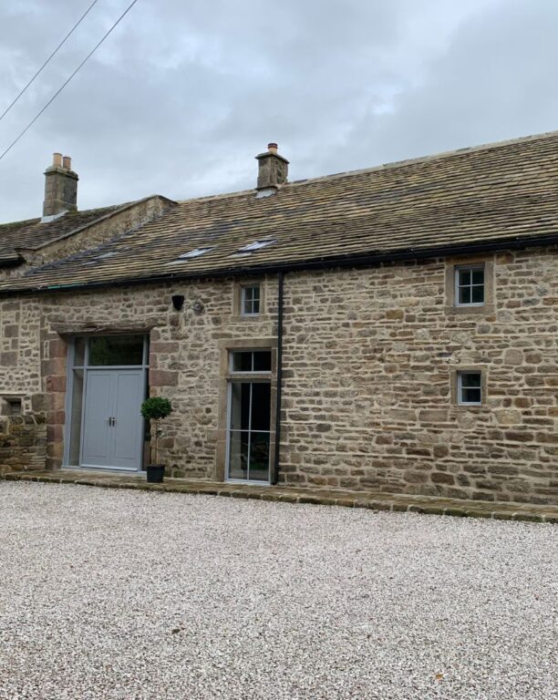 Traditional stone cottage with grey doors and windows featuring slate roof and gravel driveway