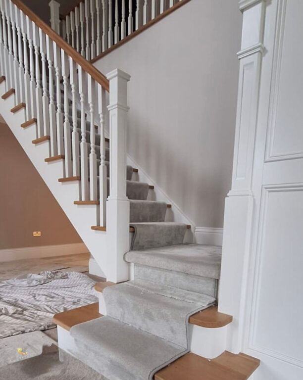 Traditional staircase with white painted spindles, oak handrail and grey carpet runner by Overgreen Joinery