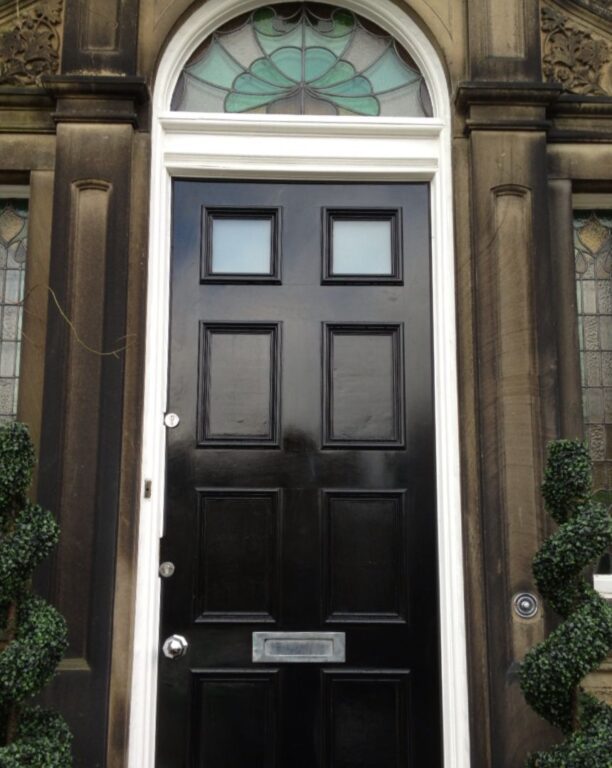 Victorian style black front door with decorative fanlight and ornate stone columns