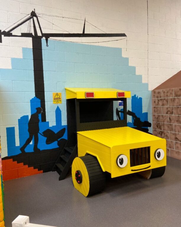 Construction themed children's playroom with digger toy and building site wall mural