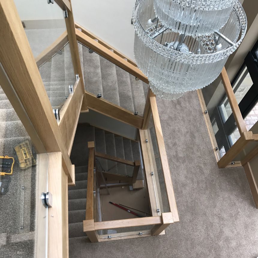Luxury oak staircase with glass balustrade and crystal chandelier viewed from above in modern Yorkshire home