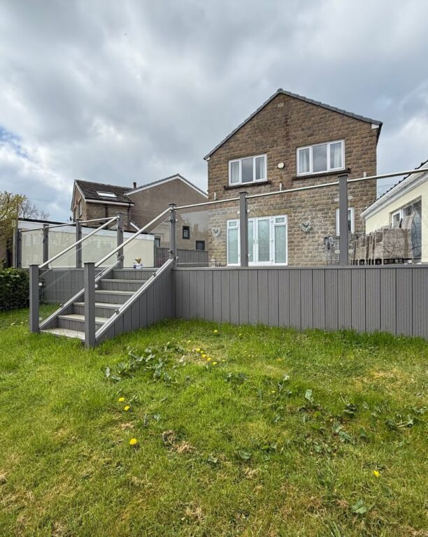 Raised composite decking with glass panel railings and steps in contemporary garden setting