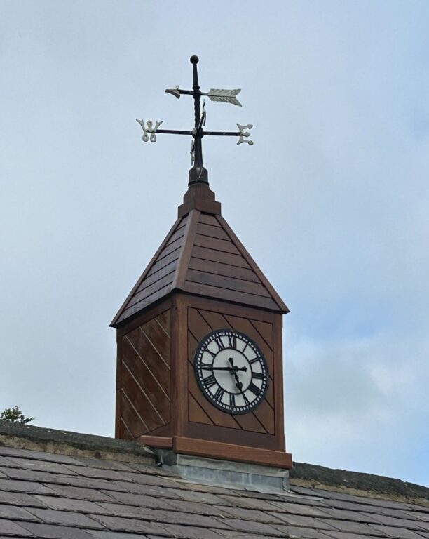 Traditional wooden clock tower with Roman numeral face and decorative weathervane
